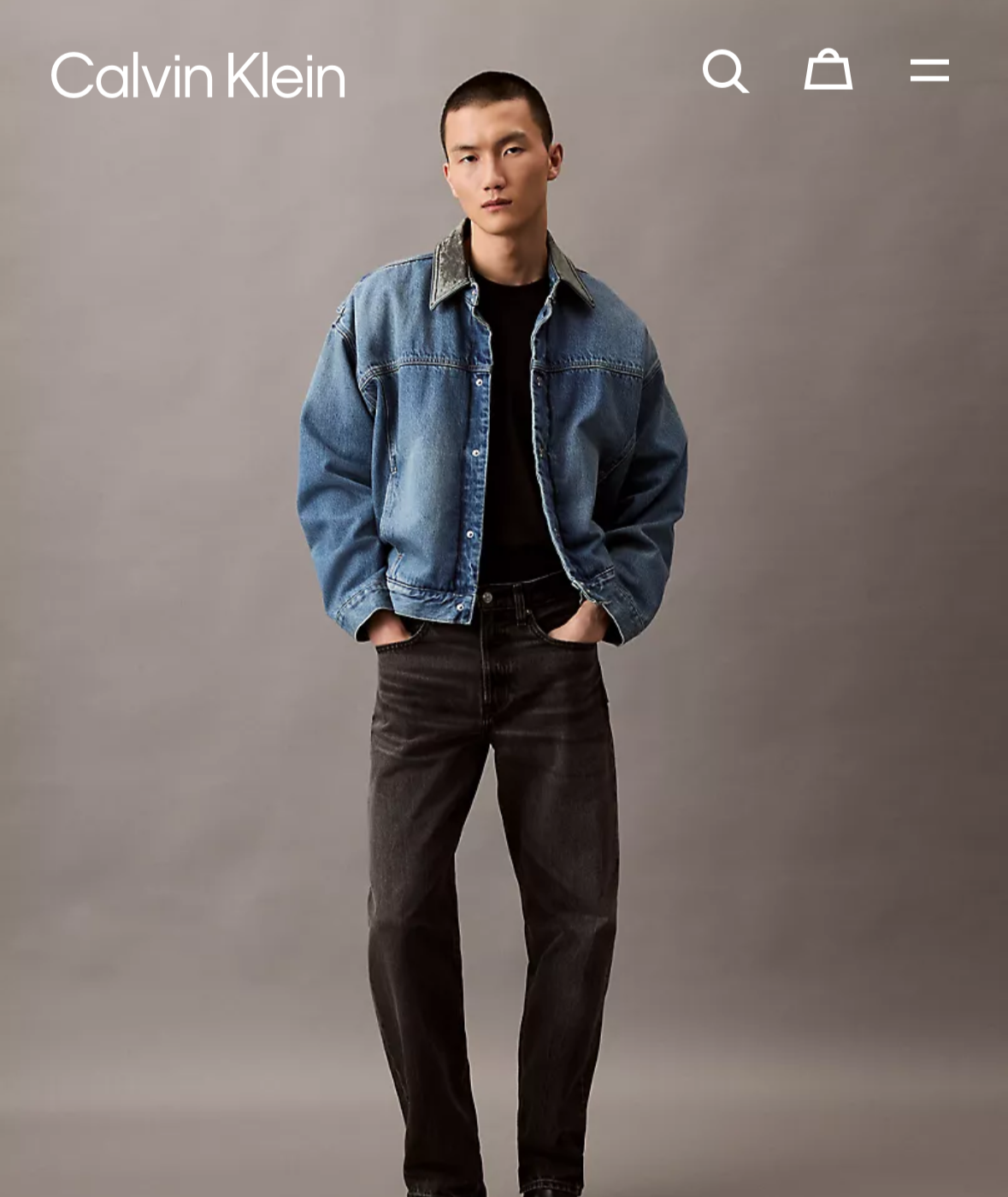 Calvin Klein clothing page on a smartphone screen with a model wearing a denim jacket and black pants.