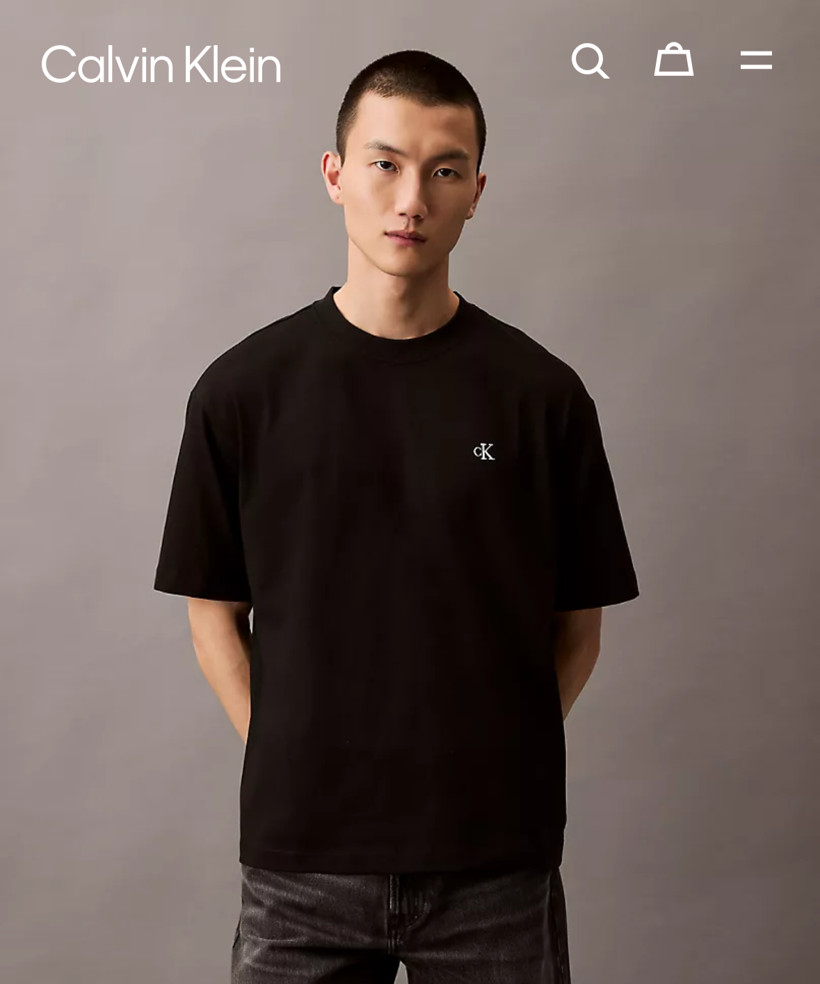 Calvin Klein product page with a model wearing a black t-shirt and pants on a gray background.